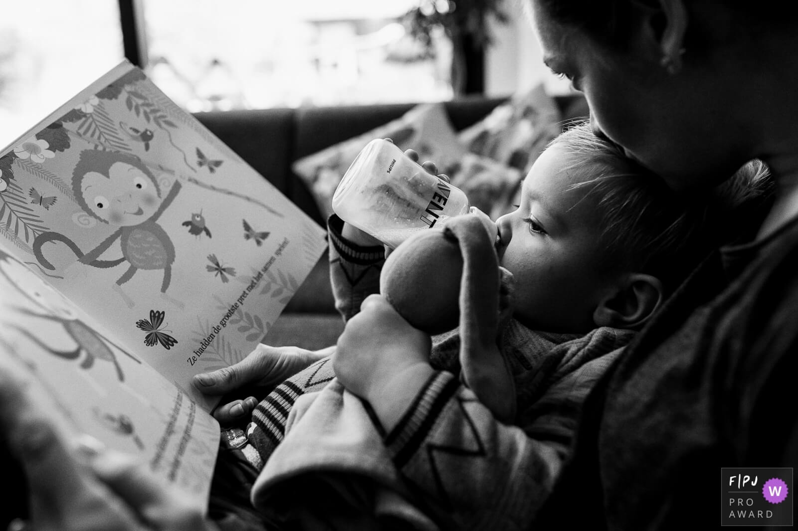 een mama leest voor uit een boekje aan haar zoon die de fles drinkt tijdens een gezinsreportage thuis