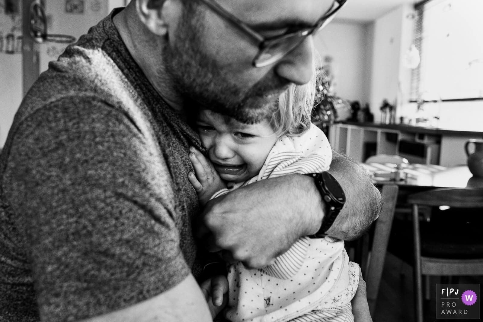 een papa knuffelt huilende dochter tijdens een gezinsreportage thuis